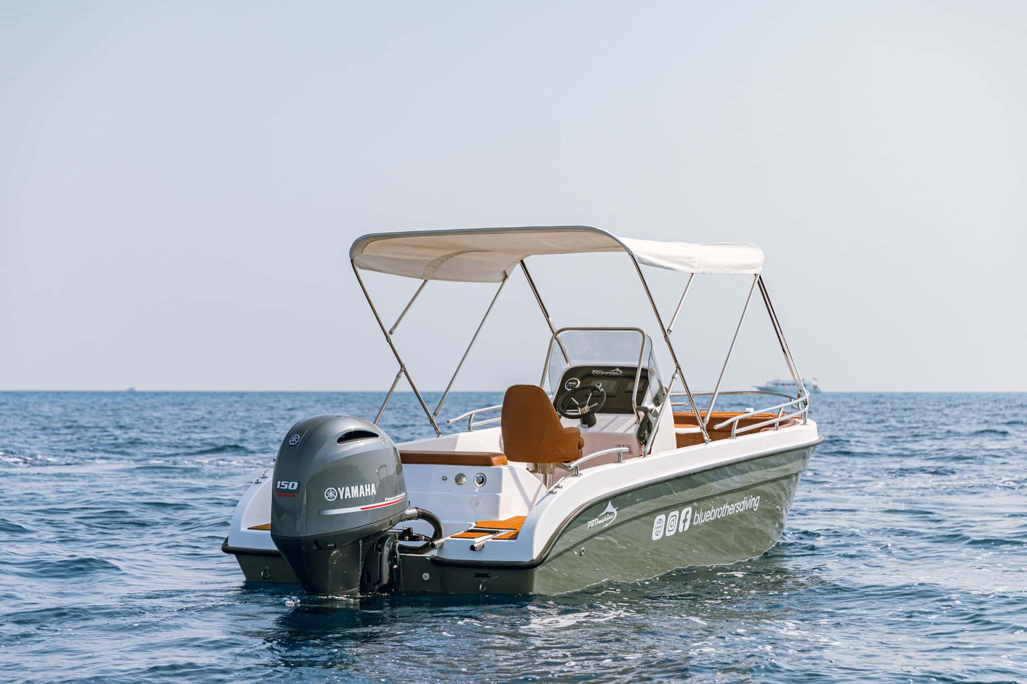 Back view of a small, green and white motorboat with a Yamaha outboard engine in blue water.