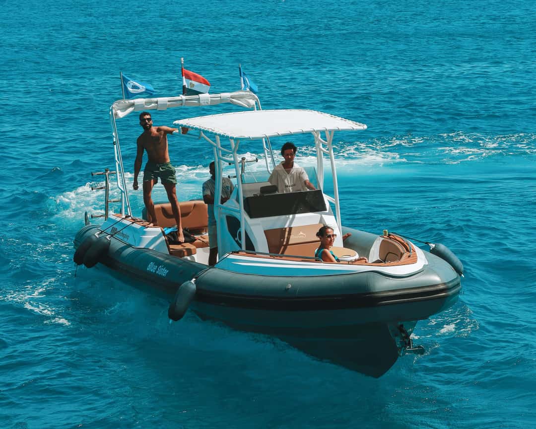 Dark grey inflatable boat with three people cruises on clear blue ocean.