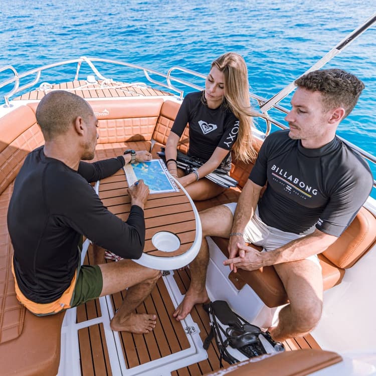 Three friends in rash guards relax on a luxury boat, enjoying the blue ocean.