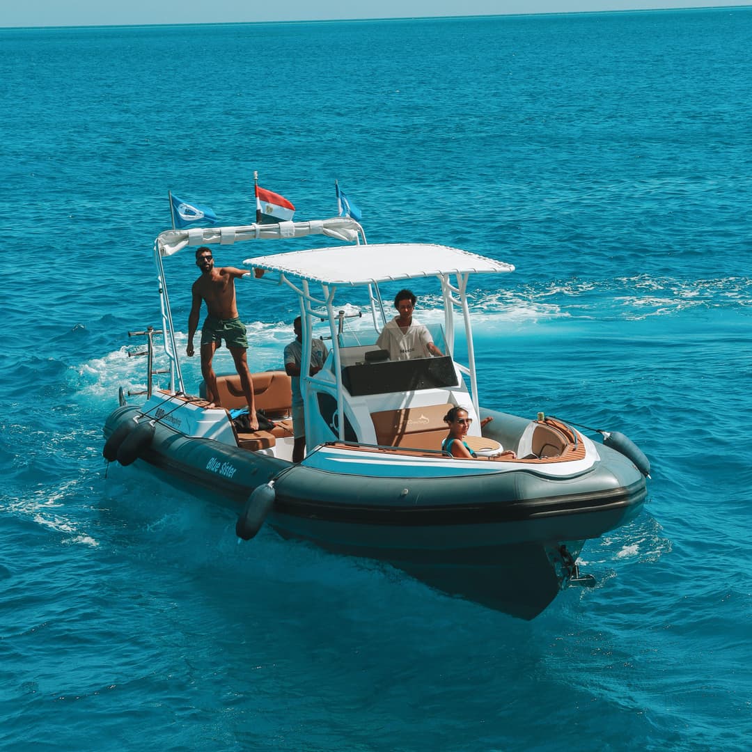 A small boat with people on board cruises on clear blue open water.