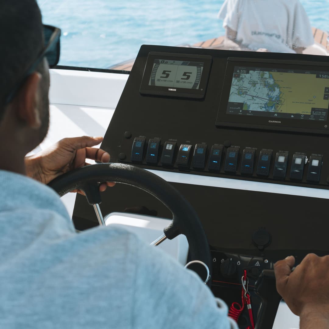 Person's hands on a boat's steering wheel and dashboard with navigation screens.
