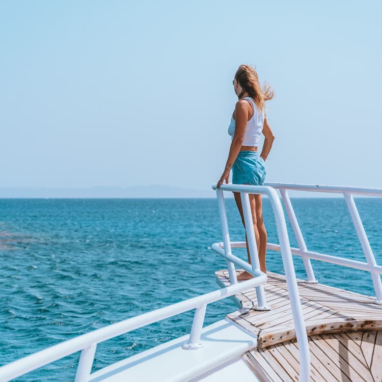 Young woman on a boat gazing at the vast blue ocean under a clear sky.