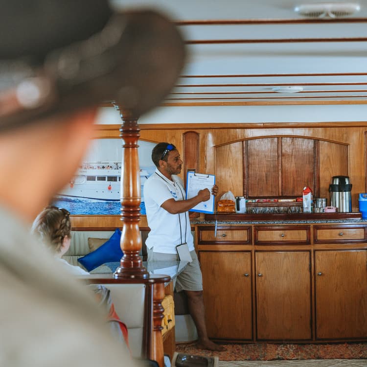 A man on a boat presents a document to an audience from behind.