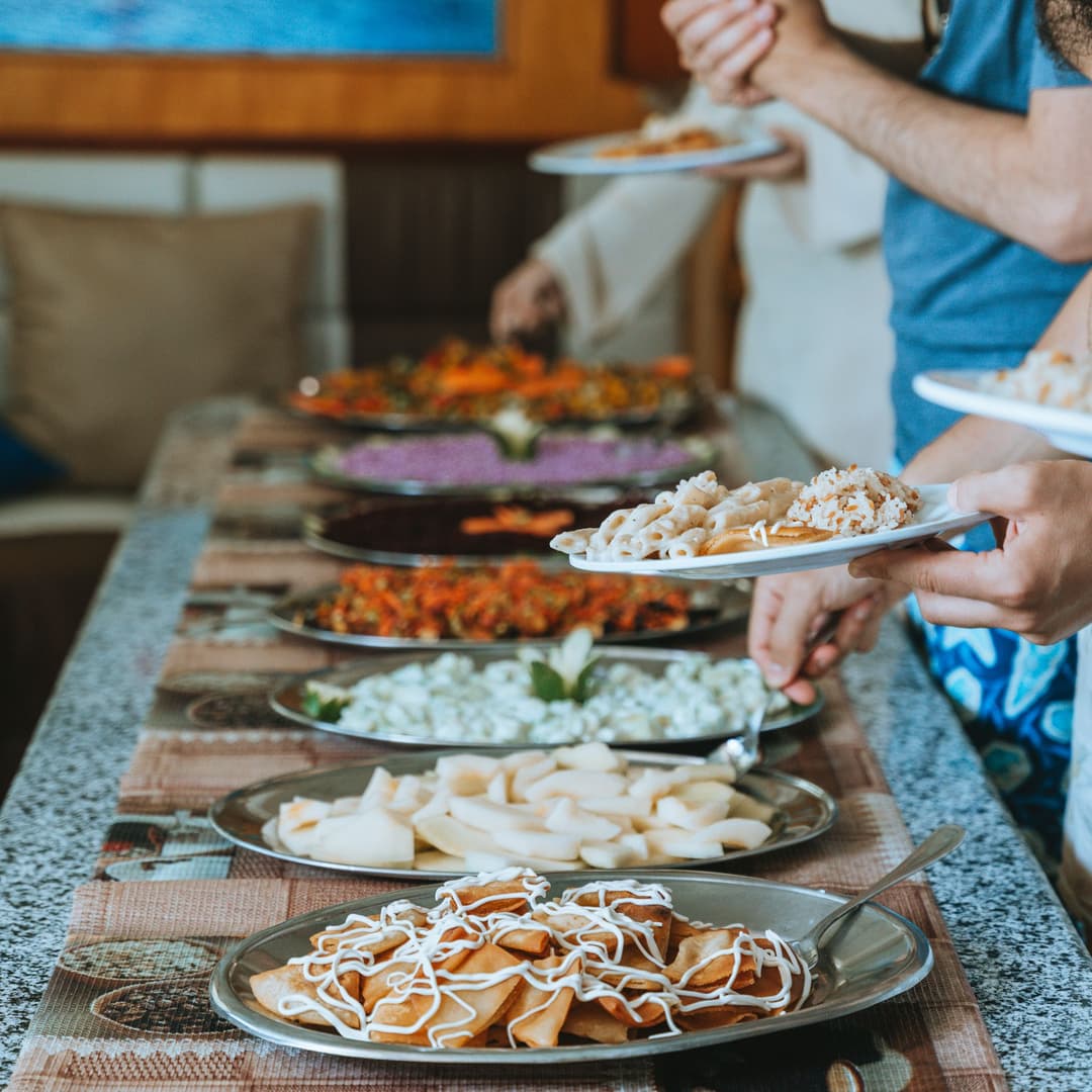 People serving themselves from a buffet table laden with a variety of colorful dishes.