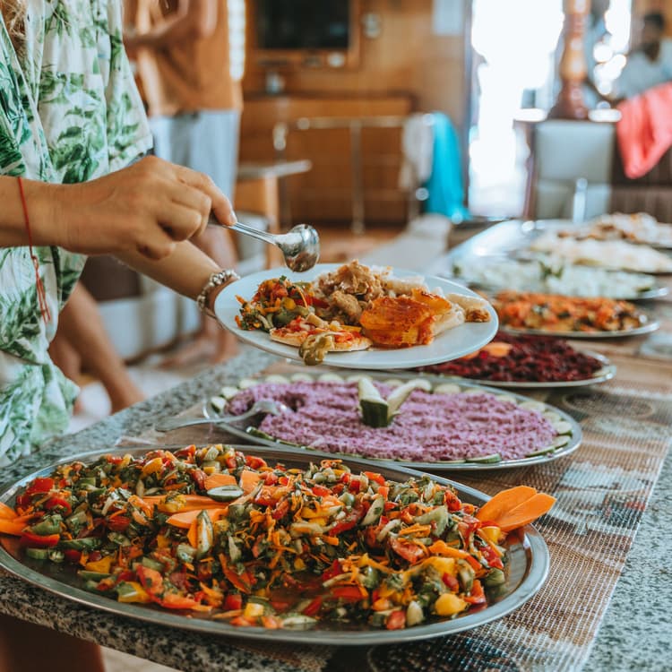 Hands reaching for food from a vibrant and diverse buffet spread on a table.