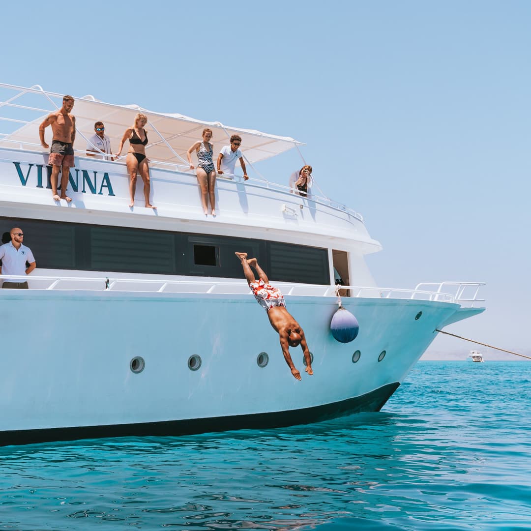 Person diving headfirst from a white yacht named VIANNA into clear turquoise water.