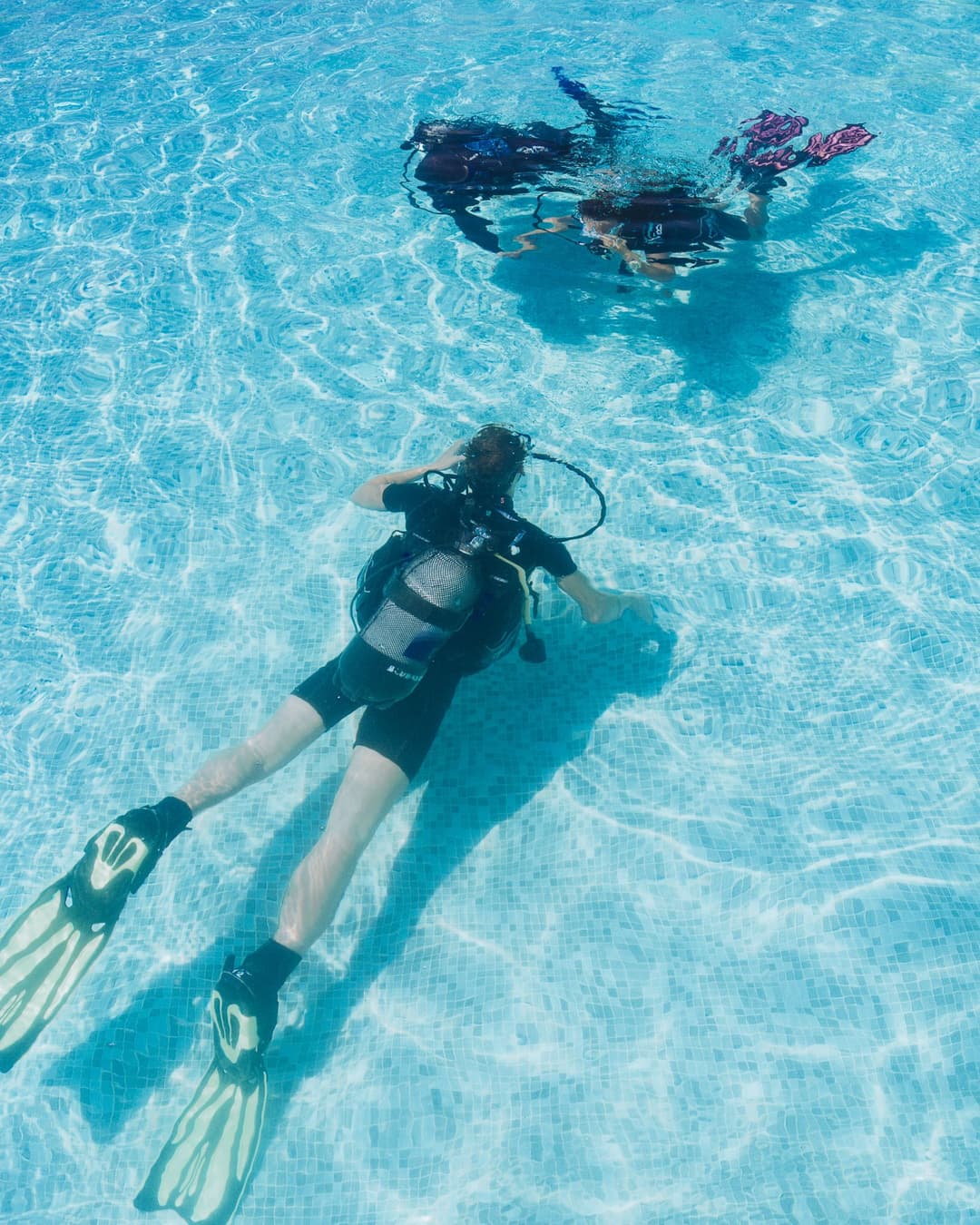 Two divers fully submerged in a clear blue swimming pool, practicing underwater techniques.