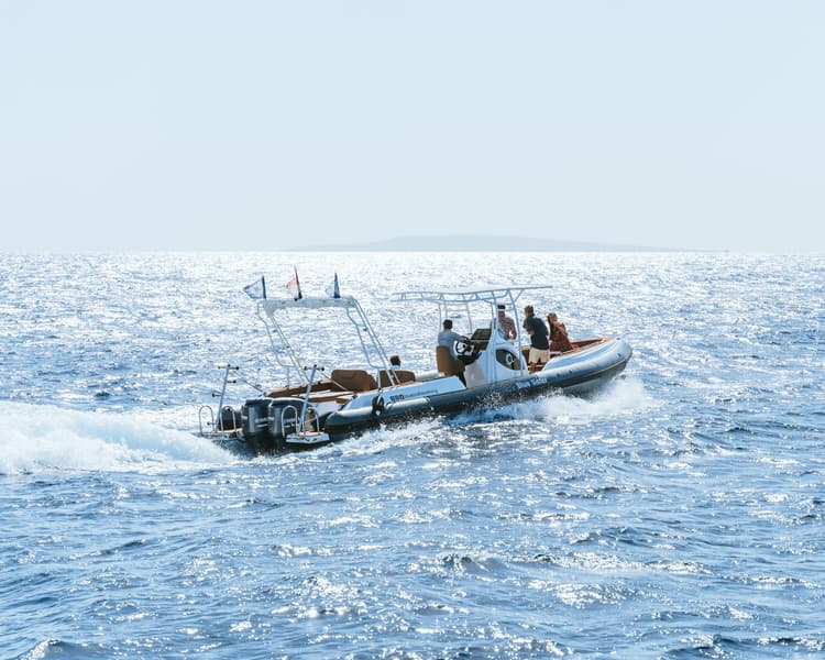 A black and white rigid inflatable boat (RIB) with several people speeding across choppy blue water.