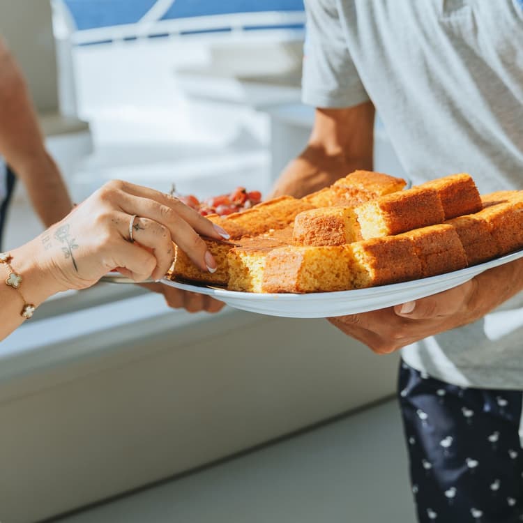 Person offering slices of golden French toast on a white plate to another person.