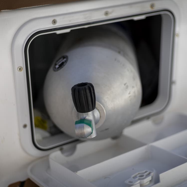 A gray scuba tank stored neatly inside a white compartment on a boat.