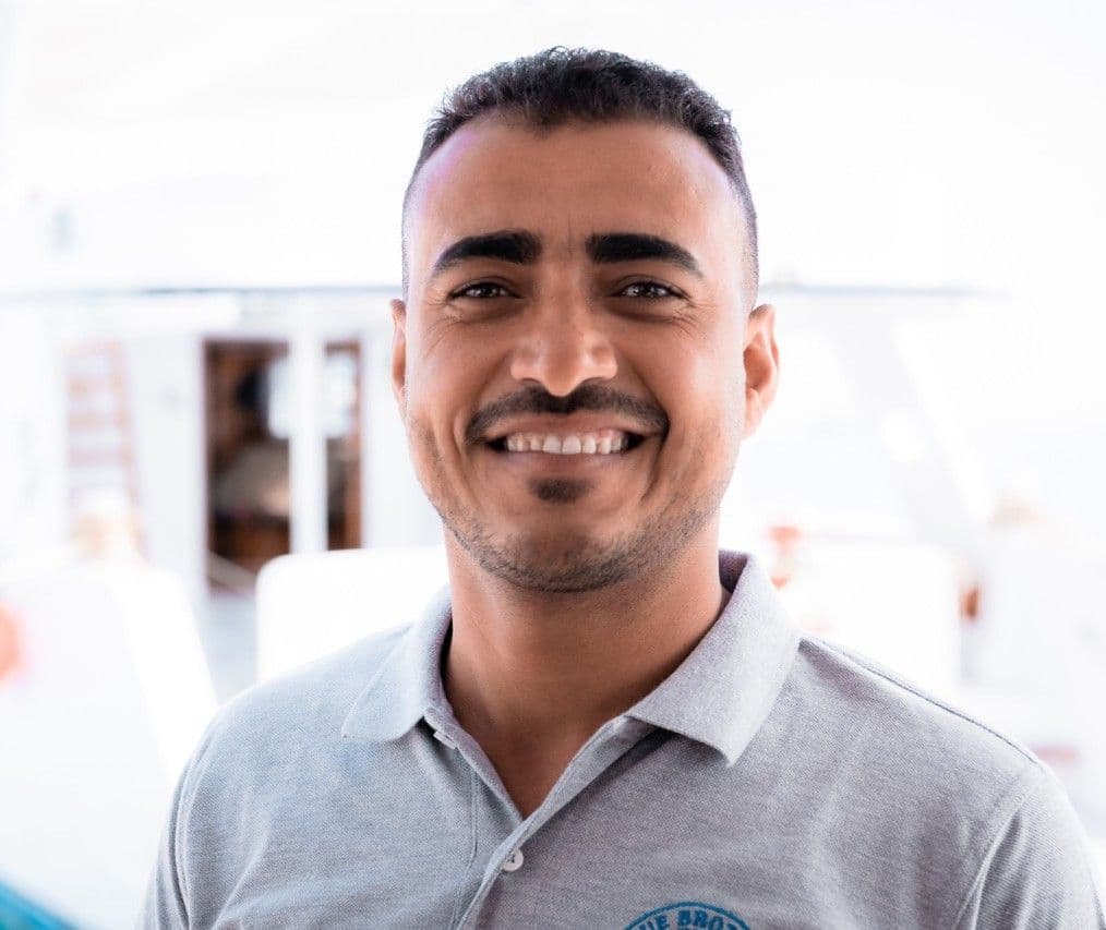 Smiling man with short dark hair and beard wearing a grey polo shirt.