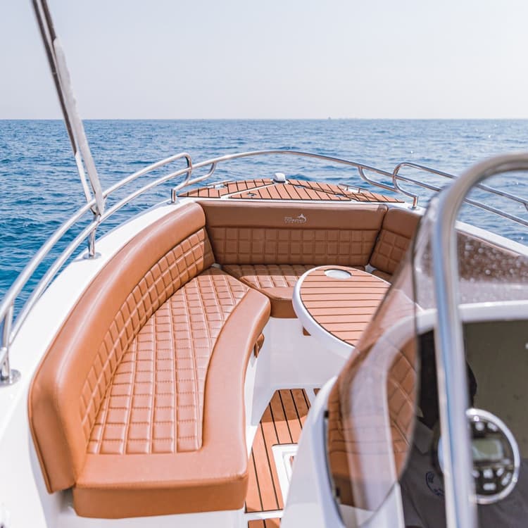 Front deck of a luxury motorboat with brown upholstered seating on blue water.